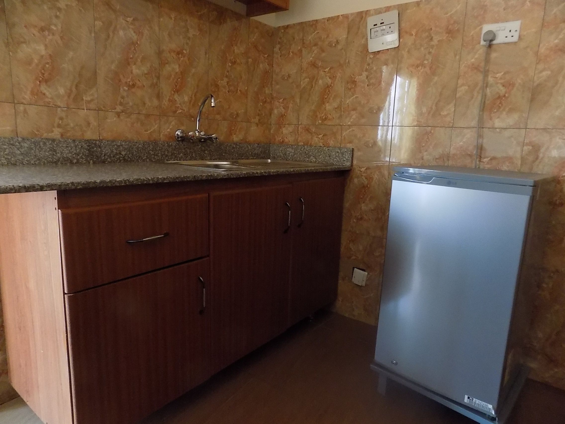 A kitchen with a sink, cabinets, and a refrigerator.