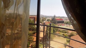 A view from a window with a metal railing, overlooking a residential area with houses and greenery. - Olina Hotel and Apartments (Kampala)