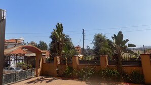 A gated residential area with a paved entrance, palm trees, and a clear blue sky. - Olina Hotel and Apartments (Kampala)
