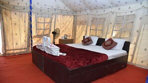 Una cama con una cubierta roja, almohadas blancas y cabecera de madera en una habitación con cortinas estampadas y alfombra roja.