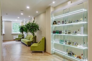 A modern lobby with green armchairs, a large potted plant, and a glass display case with various bottles. - Hotel G9 (Zelenogorsk)