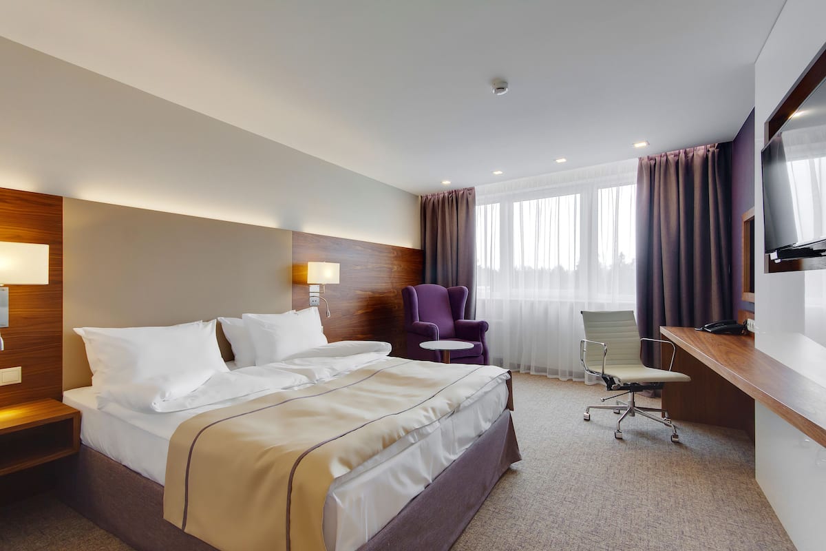A hotel room with a large bed, a desk, a chair, and a TV.