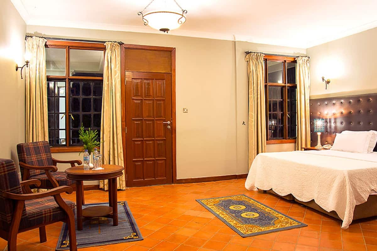 A hotel room with a bed, a chair, a small table, and a window with curtains.