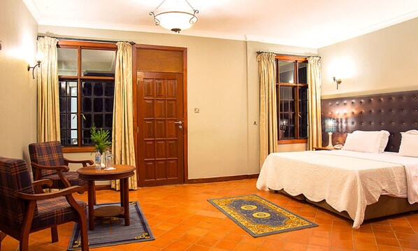 A hotel room with a bed, a chair, a small table, and a window with curtains.