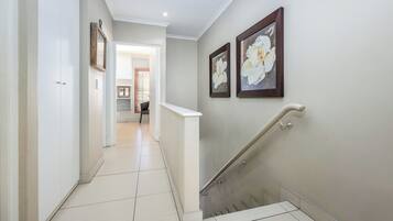 A hallway with a staircase, white walls, and two framed floral paintings.