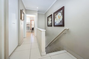 Een gang met een trap, witte wanden en twee wanddecoraties met bloemen.