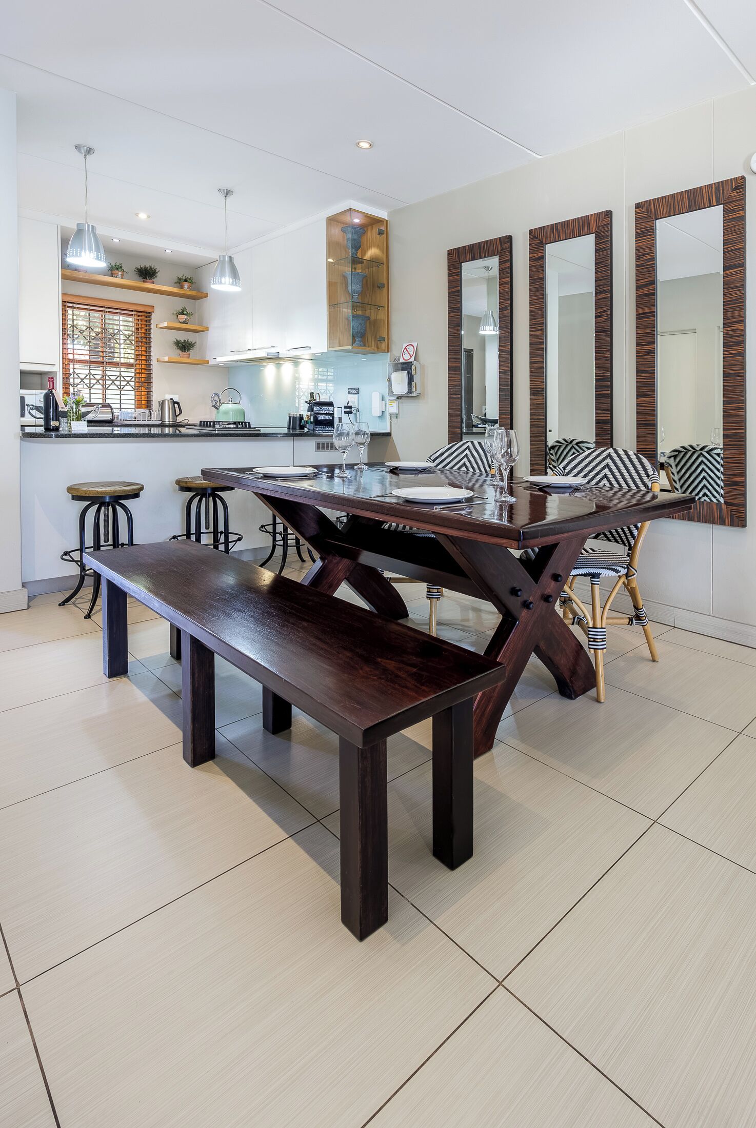 Uma cozinha moderna com área de jantar, apresentando uma mesa e cadeiras de madeira, um banco e uma ilha central com banquetas.