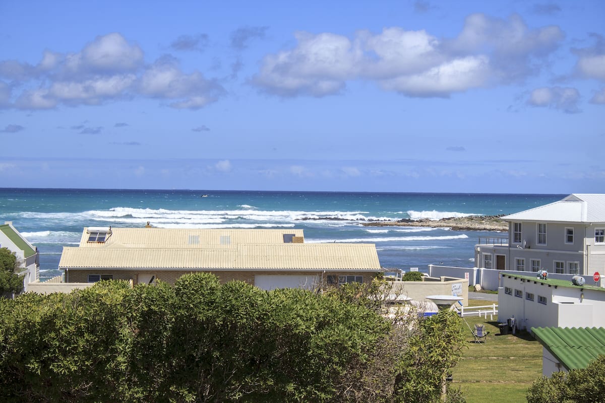 Un bâtiment situé sur la côte, doté d’un toit plat, entouré de verdure et offrant une vue sur l’océan.