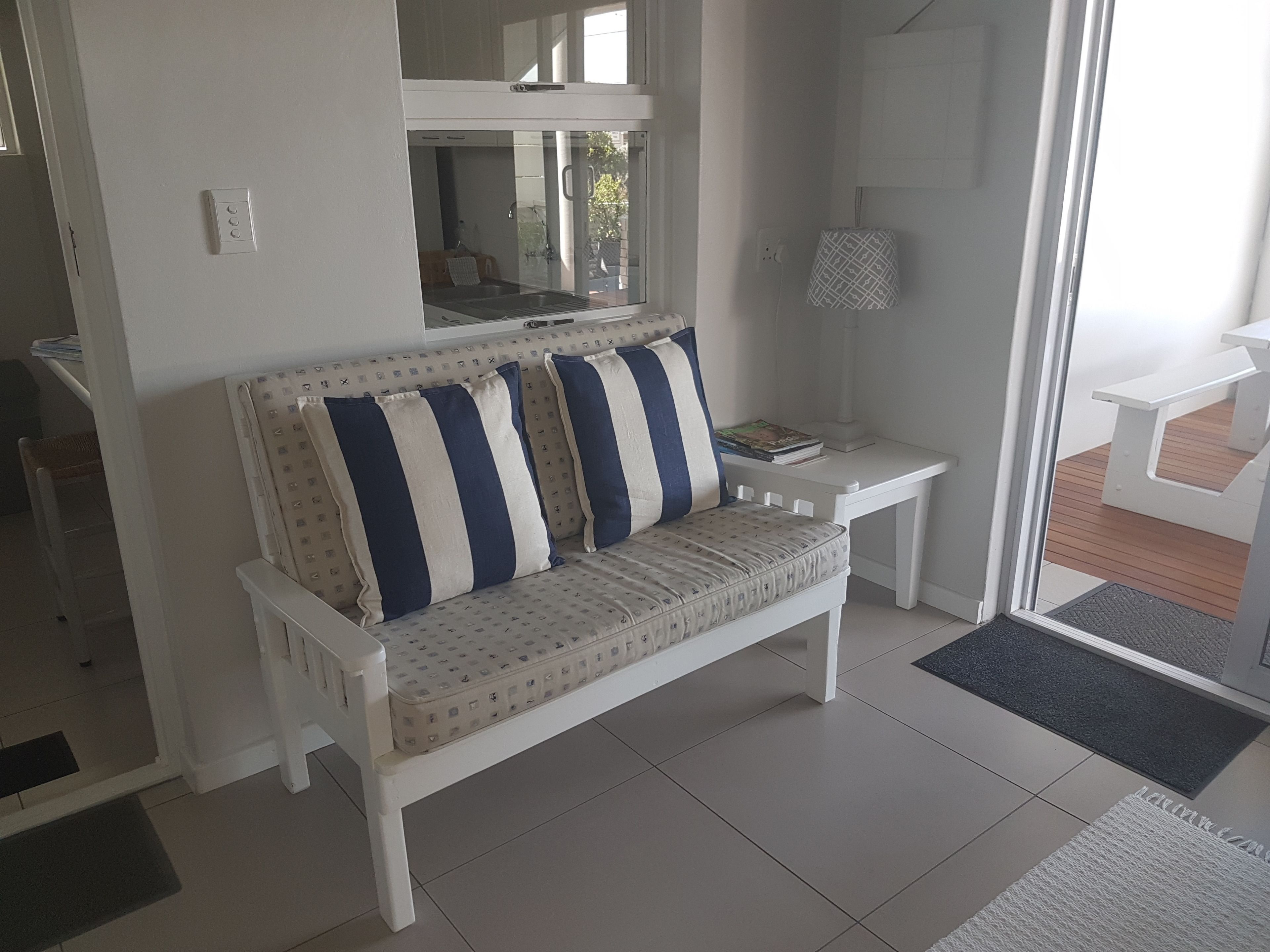 A white sofa with blue and white striped cushions, a small white side table, and a glass door leading to an outdoor area.