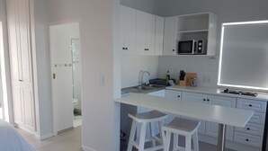A modern kitchen with white cabinets, a microwave, a sink, and a dining area with stools.