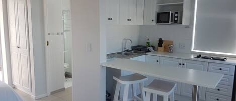 A modern kitchen with white cabinets, a microwave, a sink, and a dining area with stools.