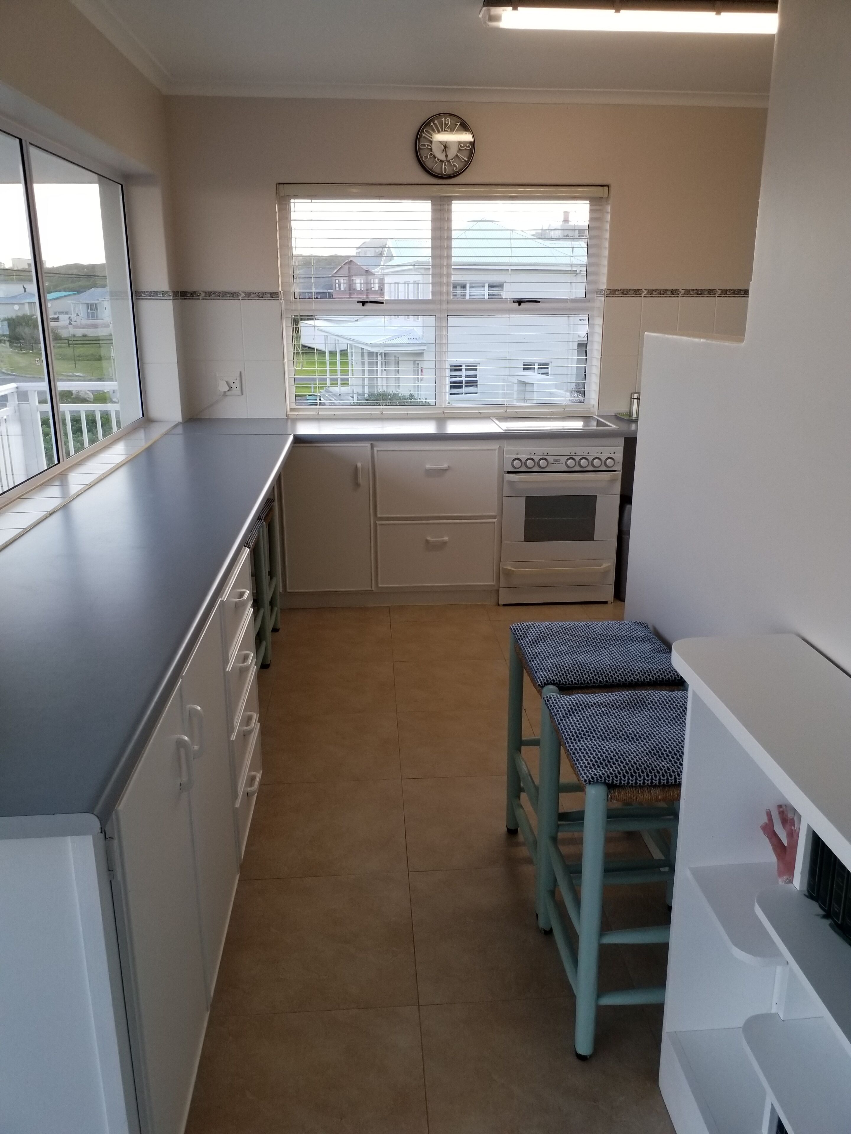 Una cocina con ventana, reloj, estufa y lavabo.