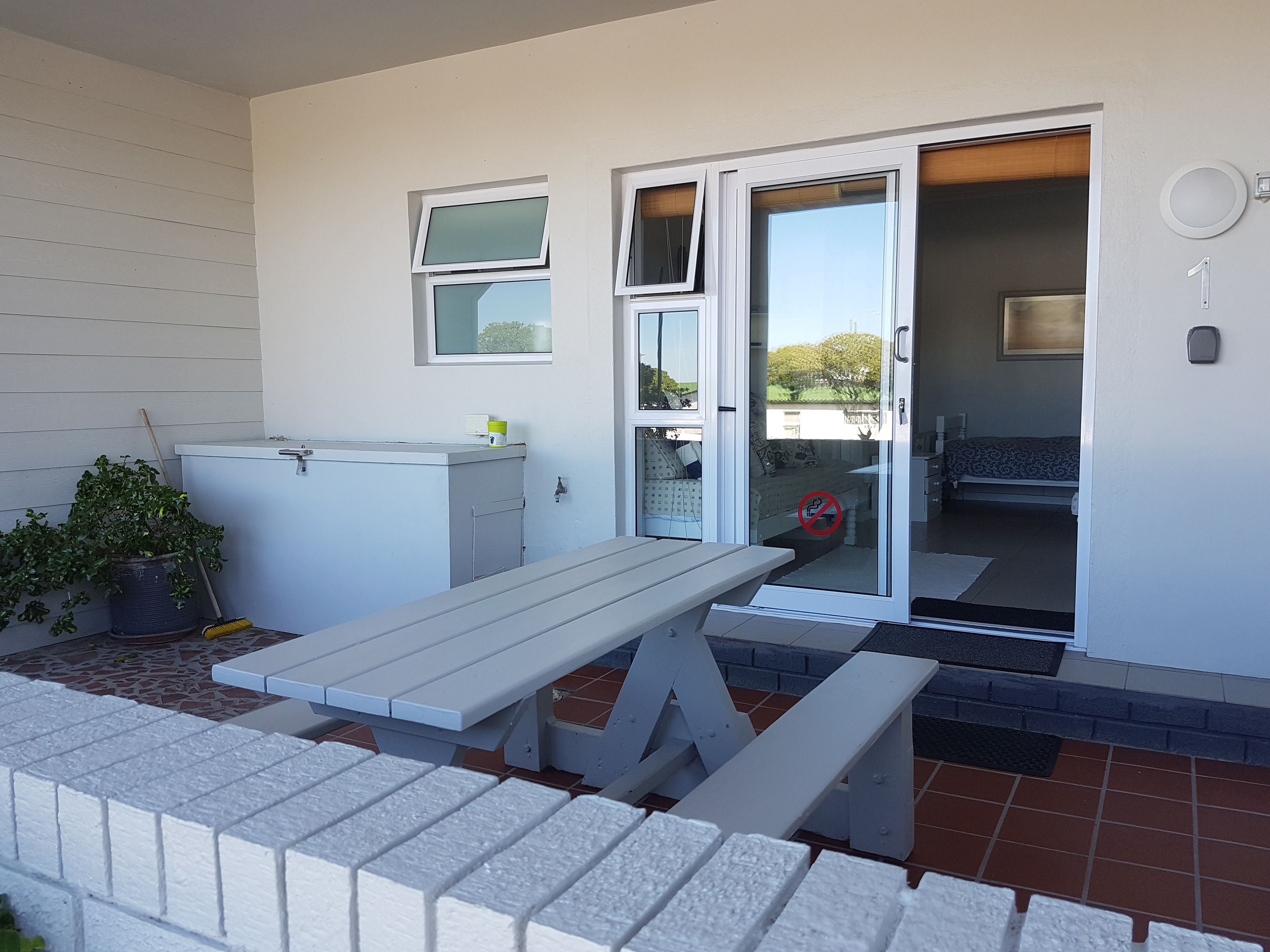 A patio with a white table and benches, a potted plant, and a utility box.