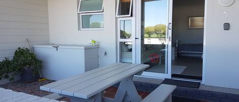 Un patio con una mesa blanca y bancos, una planta en maceta y un armario.