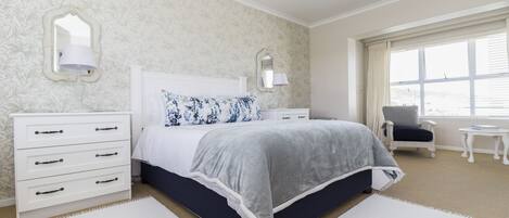 Une chambre à coucher comprenant un lit, des tables de chevet, une commode, une chaise et une fenêtre.
