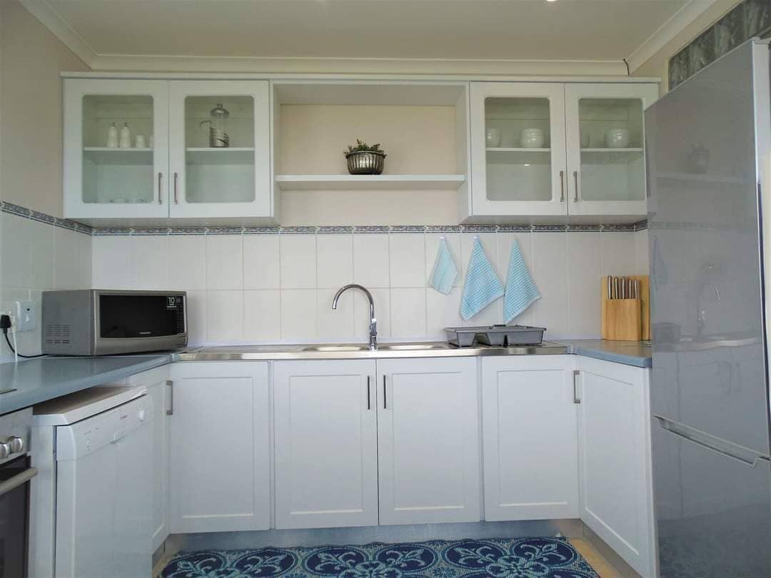 Una cocina con armarios blancos, microondas, lavabo y refrigerador.