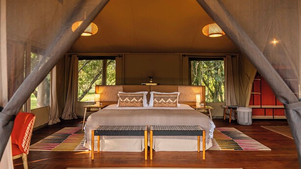 Dormitorio tipo tienda de campaña con cama, mesitas de noche y vistas al exterior.