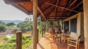 Una terraza de madera con mobiliario exterior, vista al río y un área cubierta con vistas al paisaje.
