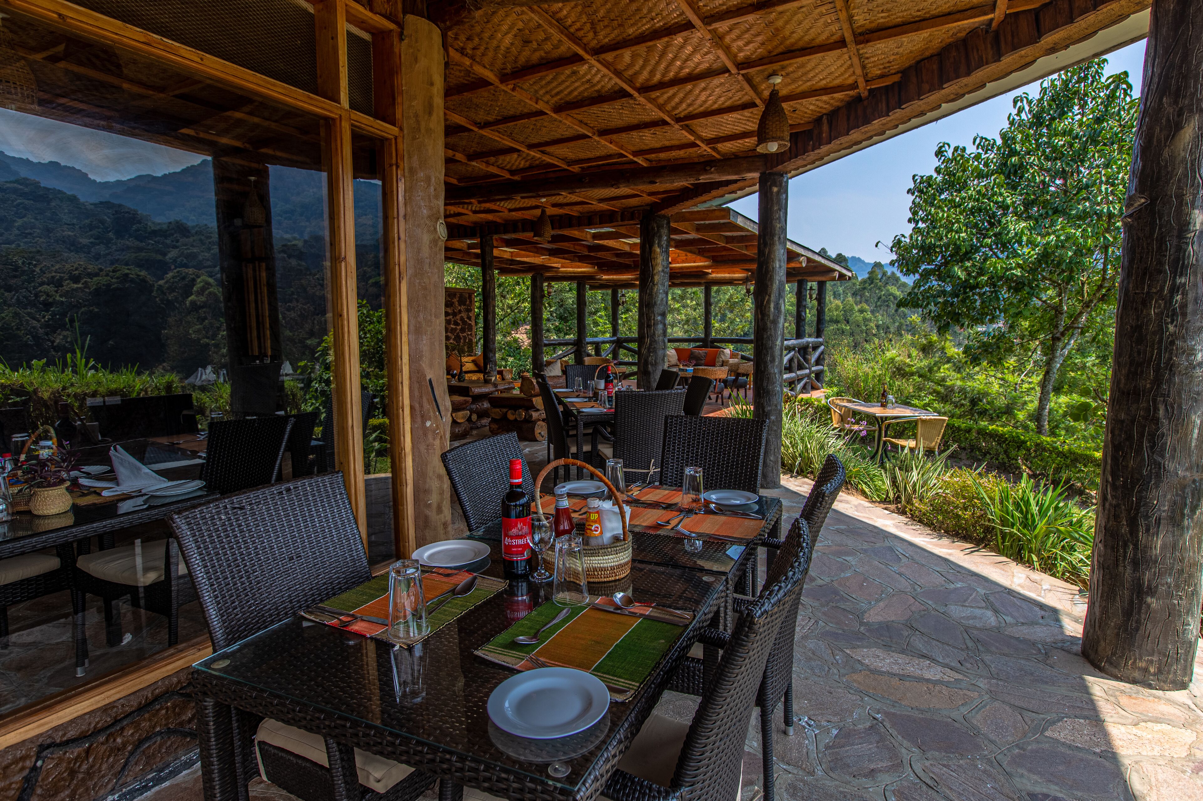 An outdoor dining area with wicker furniture, glass tables, and a view of the mountains.