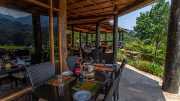 An outdoor dining area with wicker furniture, glass tables, and a view of the mountains.