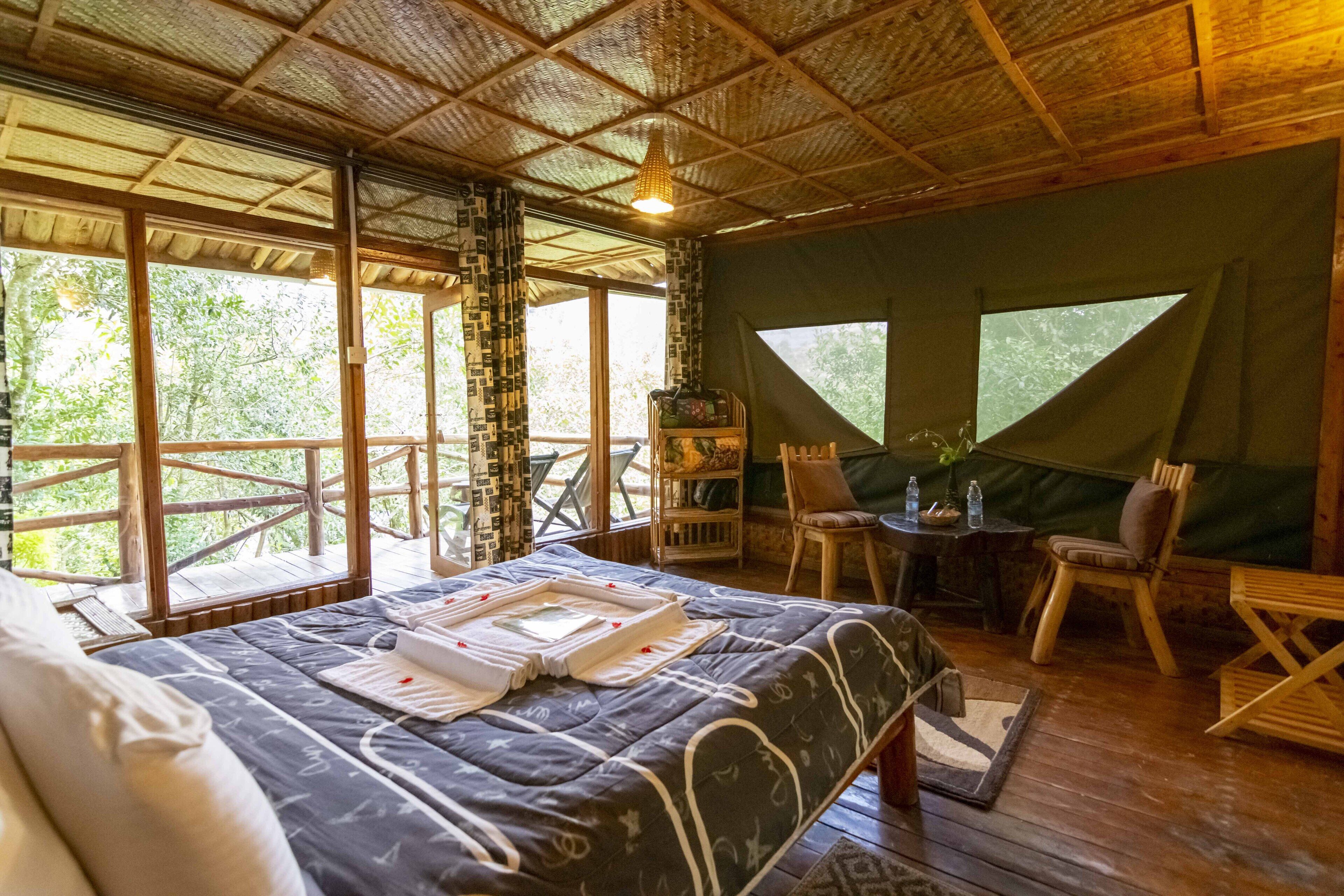 Una habitación amplia con una cama grande, una mesita con sillas y vistas al exterior a través de ventanas grandes.