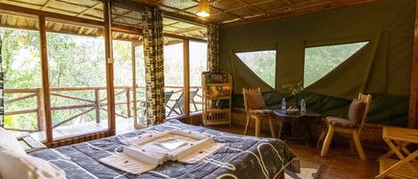 Une pièce spacieuse avec un grand lit, une petite table avec des chaises et une vue sur l’extérieur grâce à de grandes fenêtres.