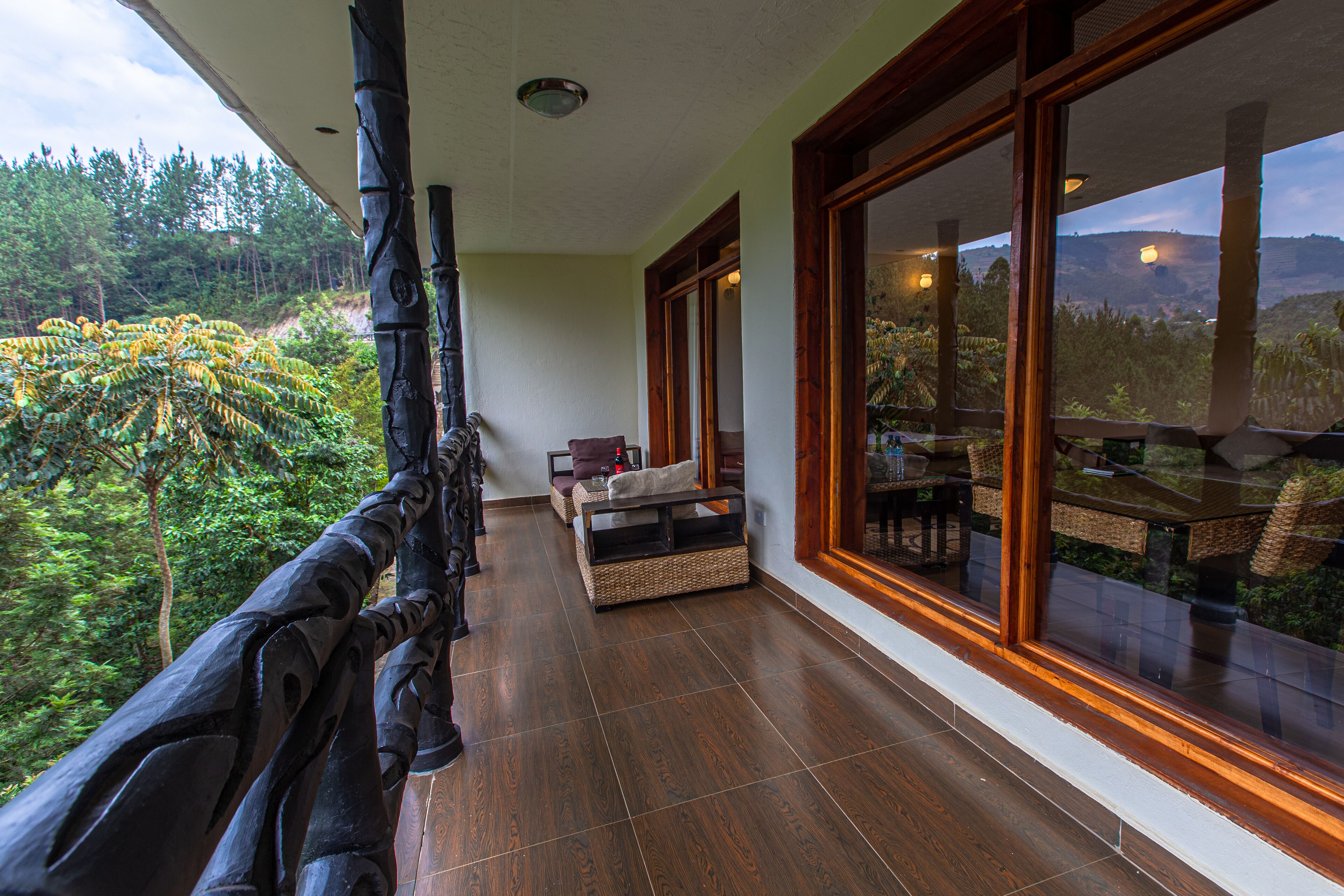 A balcony with a view of a forest, a wicker chair, and a dining table with chairs.