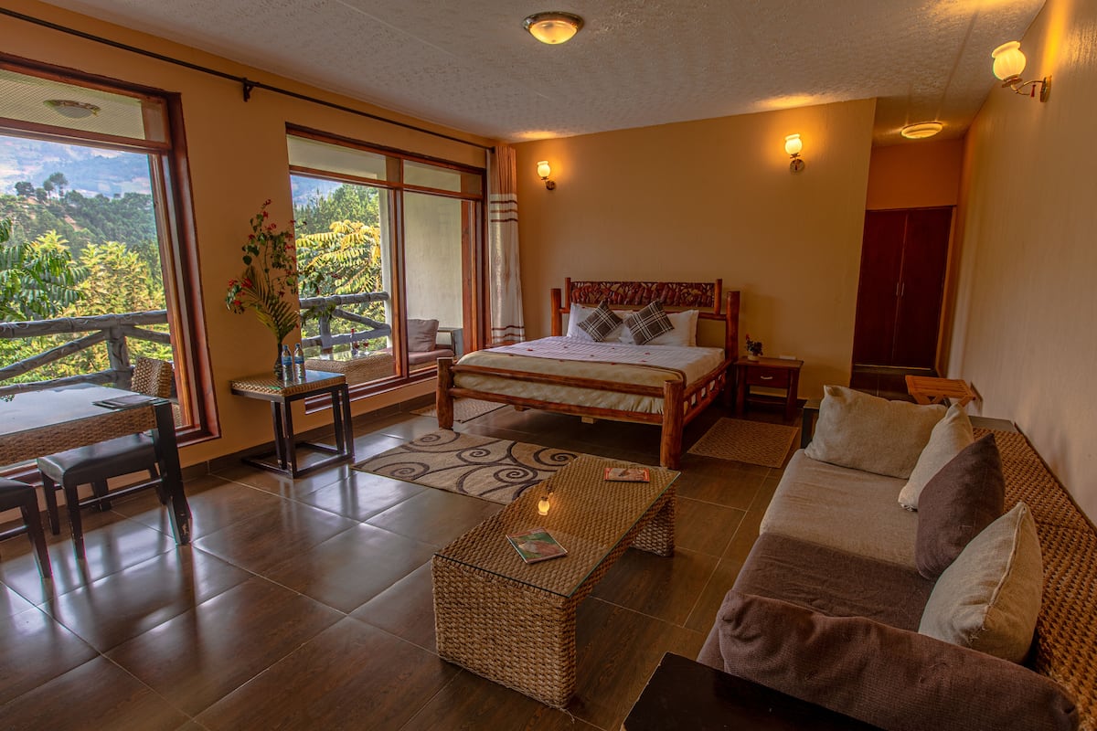 A spacious bedroom with a large bed, a sitting area with a sofa and a coffee table, and a balcony with a view of the mountains.