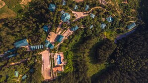 Vue aérienne d’un complexe hôtelier comprenant plusieurs bâtiments, un espace piscine central et une végétation luxuriante.