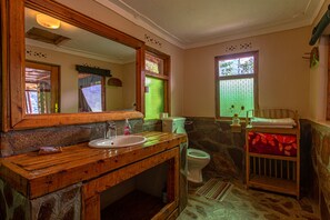 A bathroom with a wooden vanity, a sink, a toilet, and a window with a view of trees.