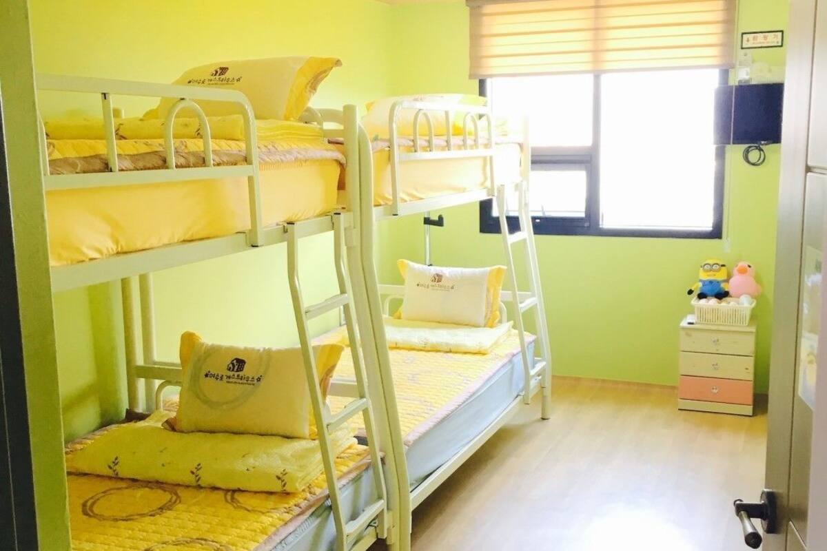 Ein Schlafraum mit Etagenbett, Fenster, Nachttisch und einem Minion Stofftier.