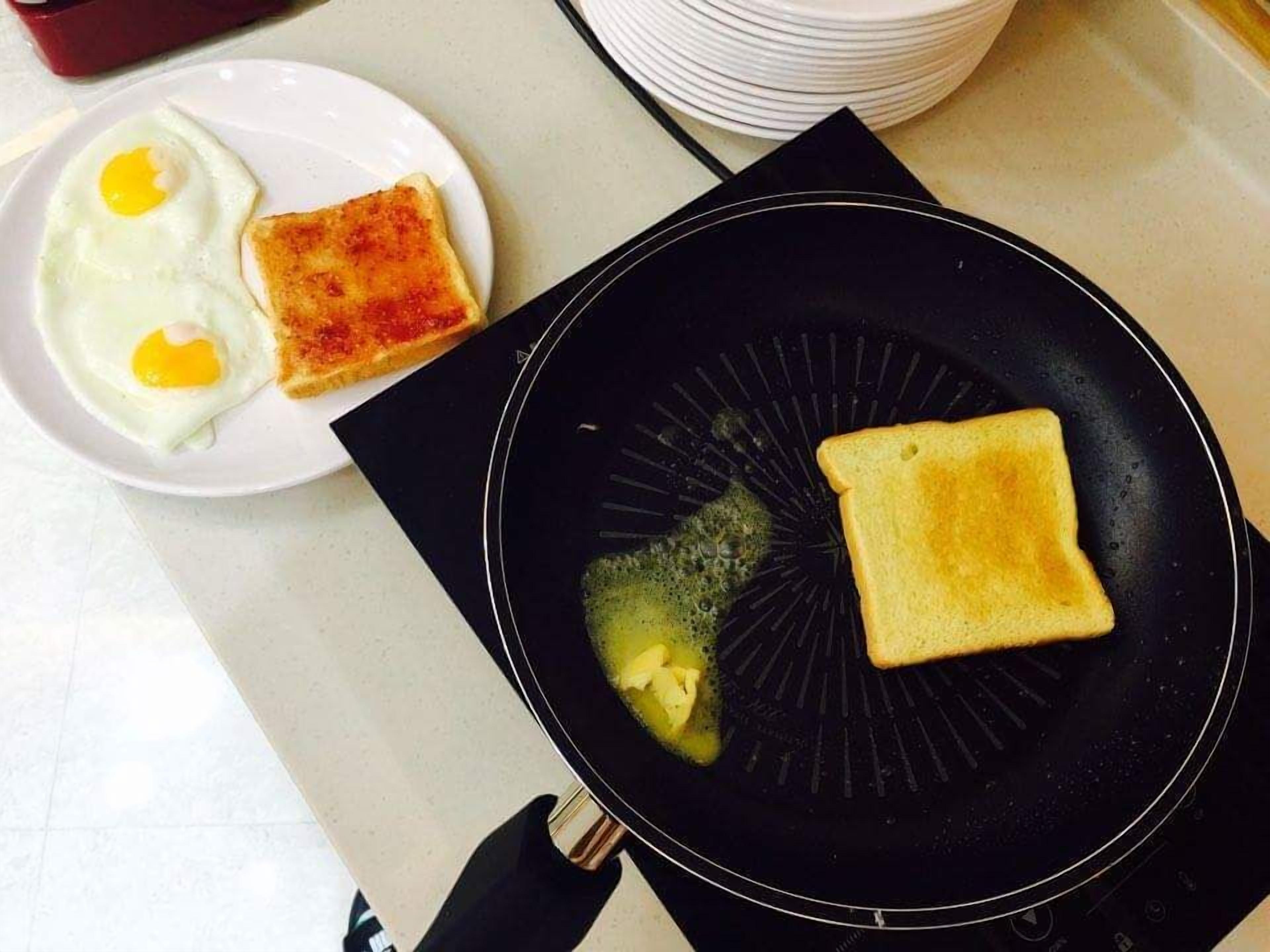 Una encimera de cocina con una sartén que contiene dos rebanadas de tostada y un plato con dos huevos fritos.