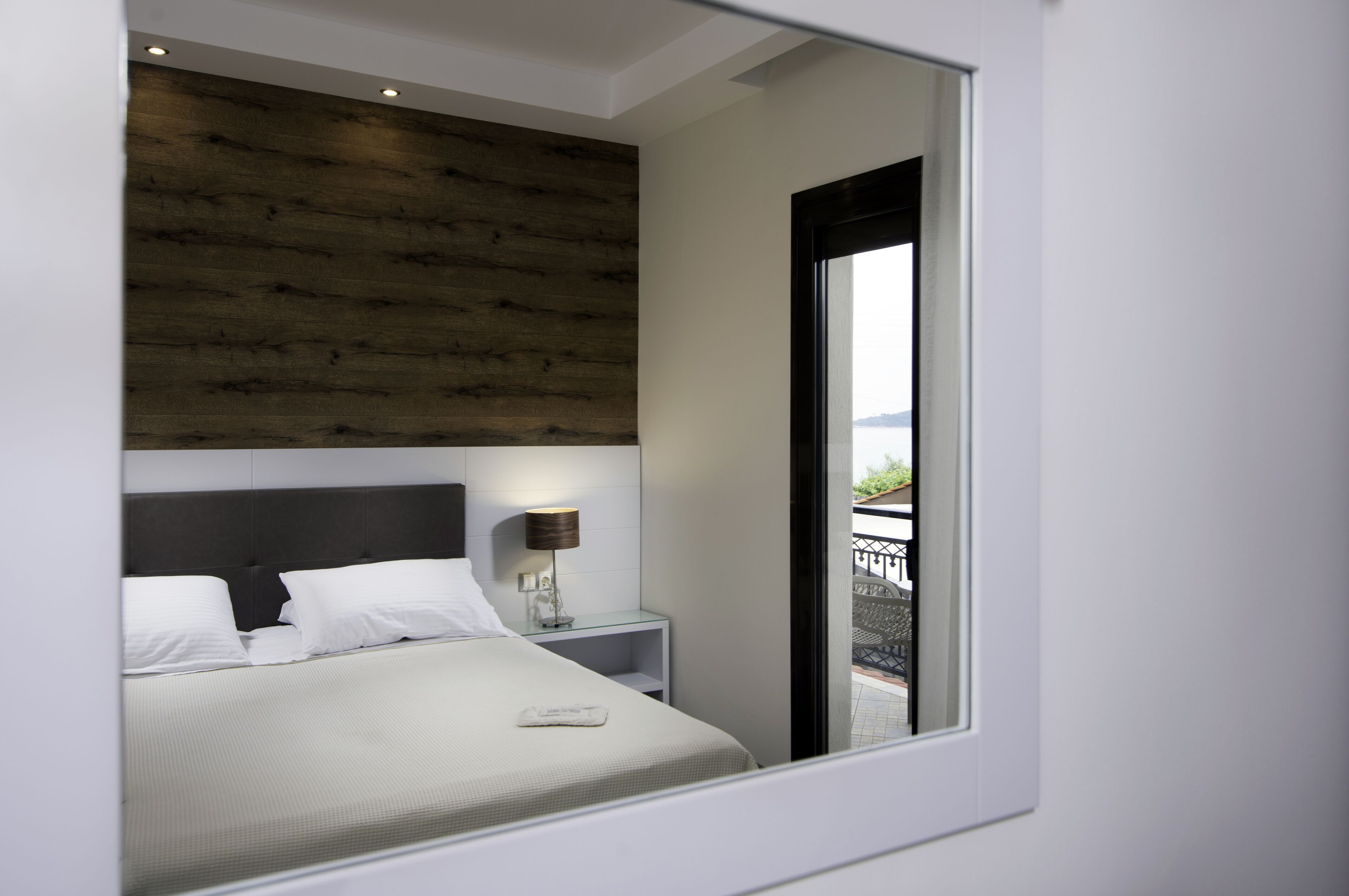 Habitación de hotel moderna con cama, mesita de noche, lámpara y vistas al balcón exterior.