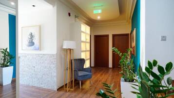 A hallway with wooden flooring, a blue chair, a standing lamp, and potted plants.