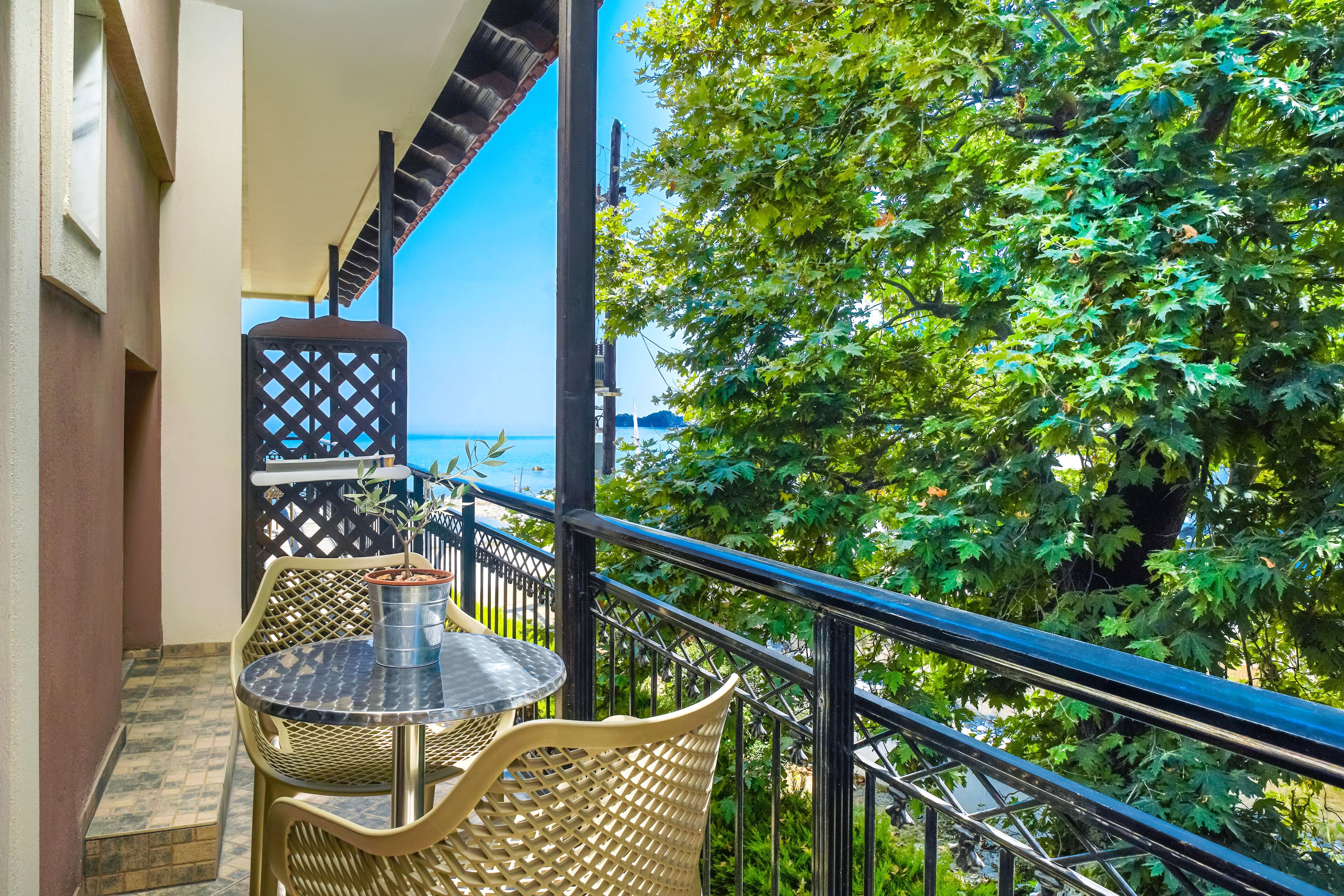 A balcony with a table and chairs, a potted plant, and a view of the sea.