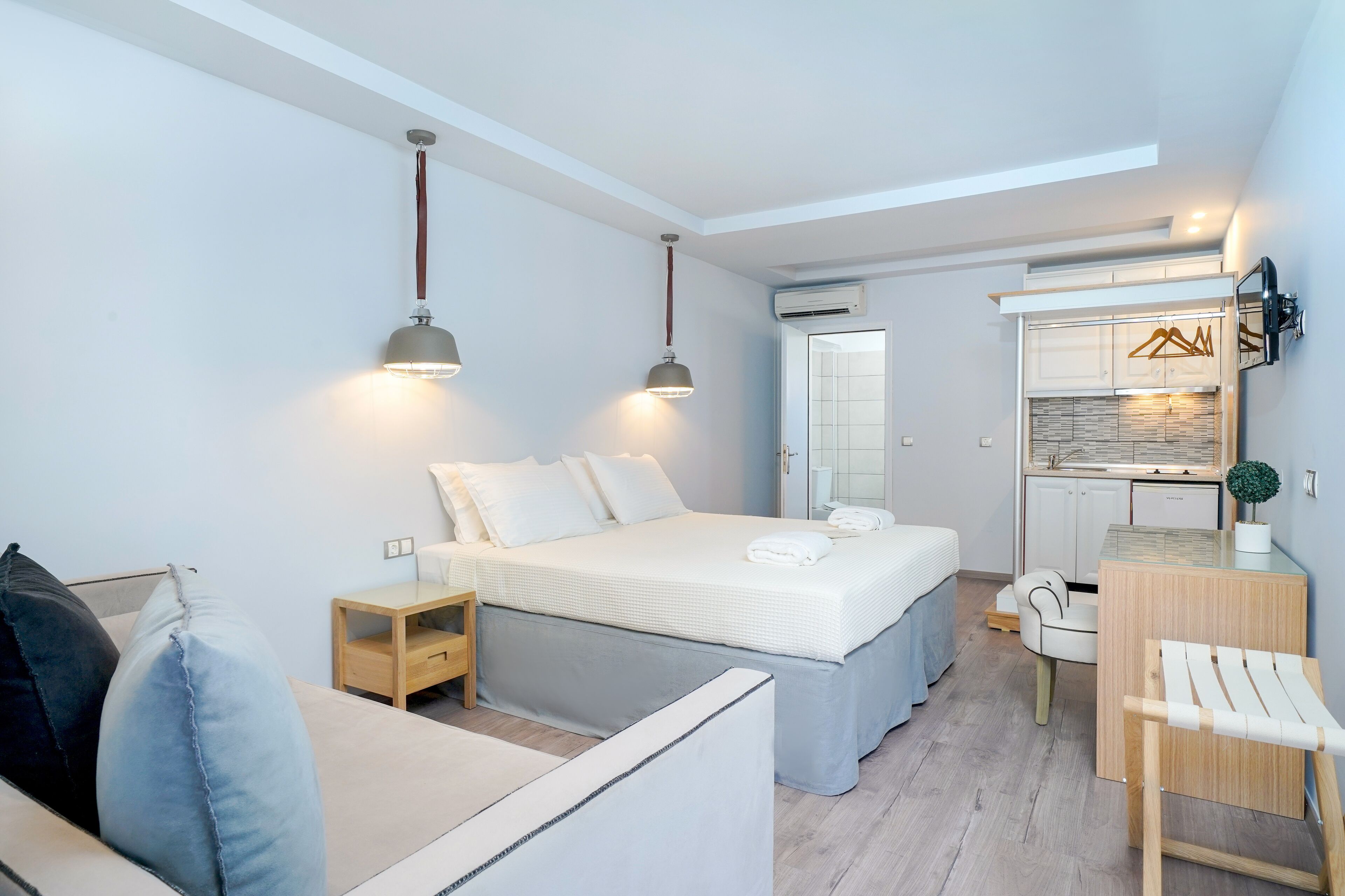 Une chambre moderne et bien éclairée, dotée d’un grand lit, de tables de chevet, d’un petit coin salon et d’une kitchenette.