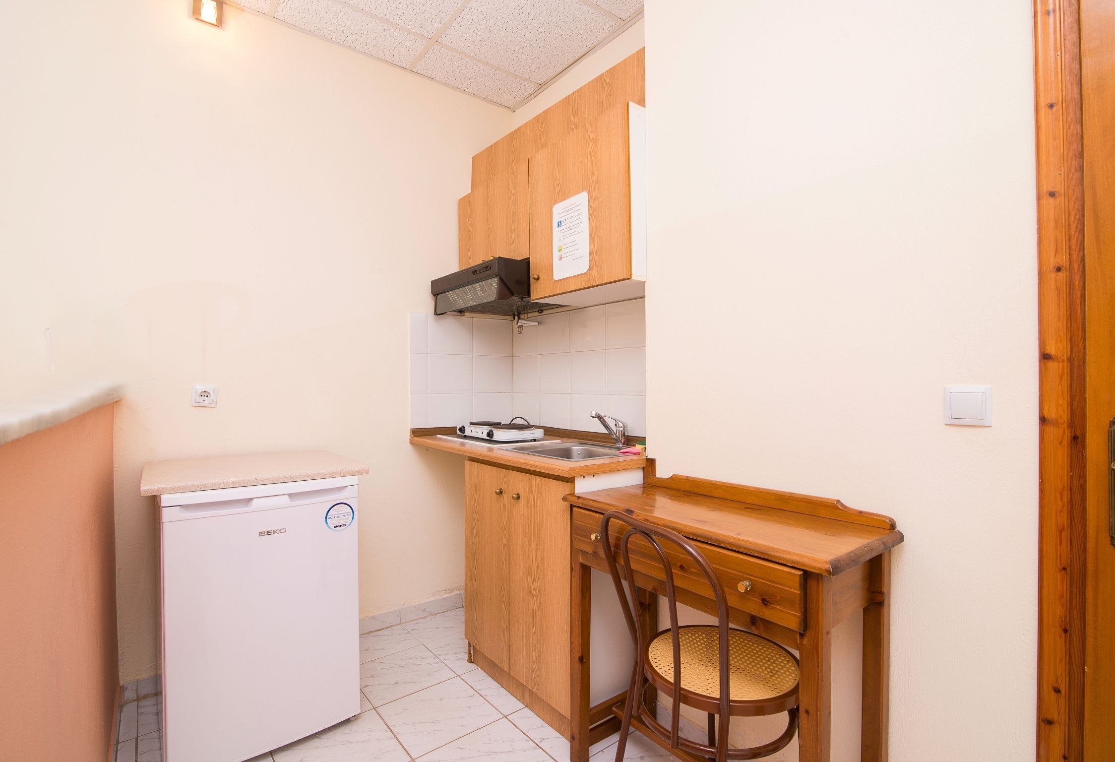 A compact kitchen with a built-in dishwasher, wooden cabinets, a small sink, and a wooden table with a chair.