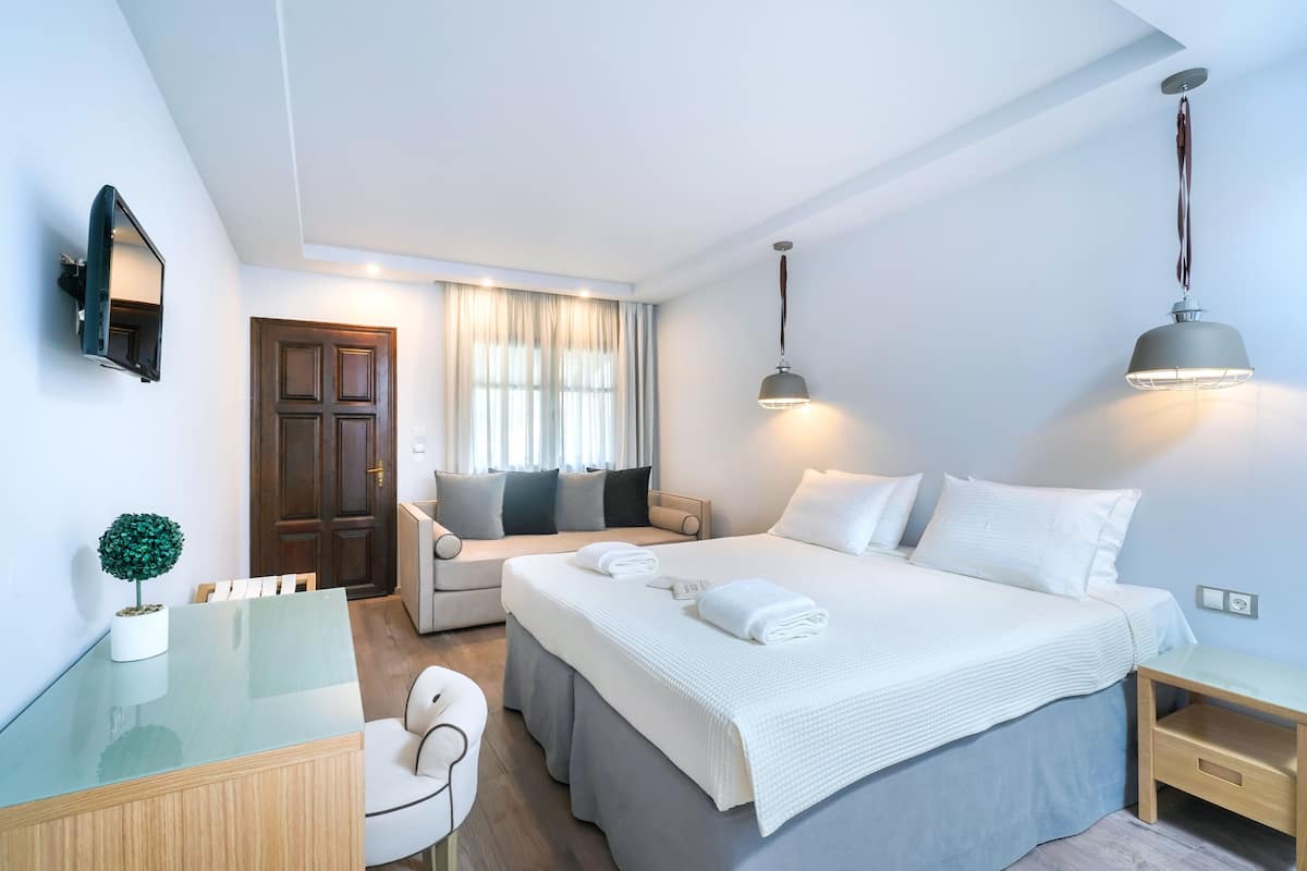 Una habitación de hotel moderna con una cama grande, mesitas de noche, un escritorio, una silla, una pequeña planta en maceta y un televisor montado en la pared.