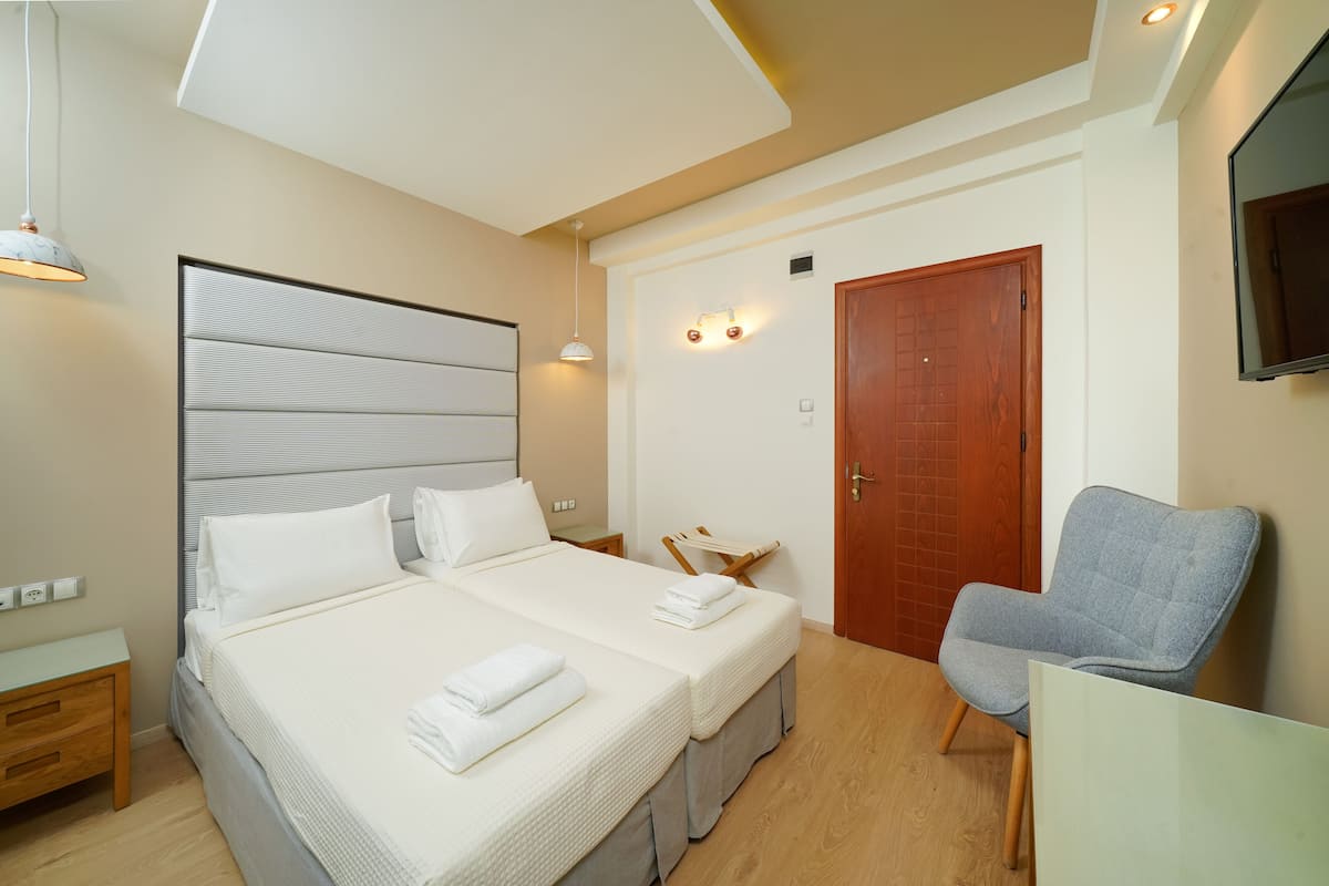 Una habitación de hotel moderna con una cama grande, mesitas de noche, una silla y un televisor en la pared.