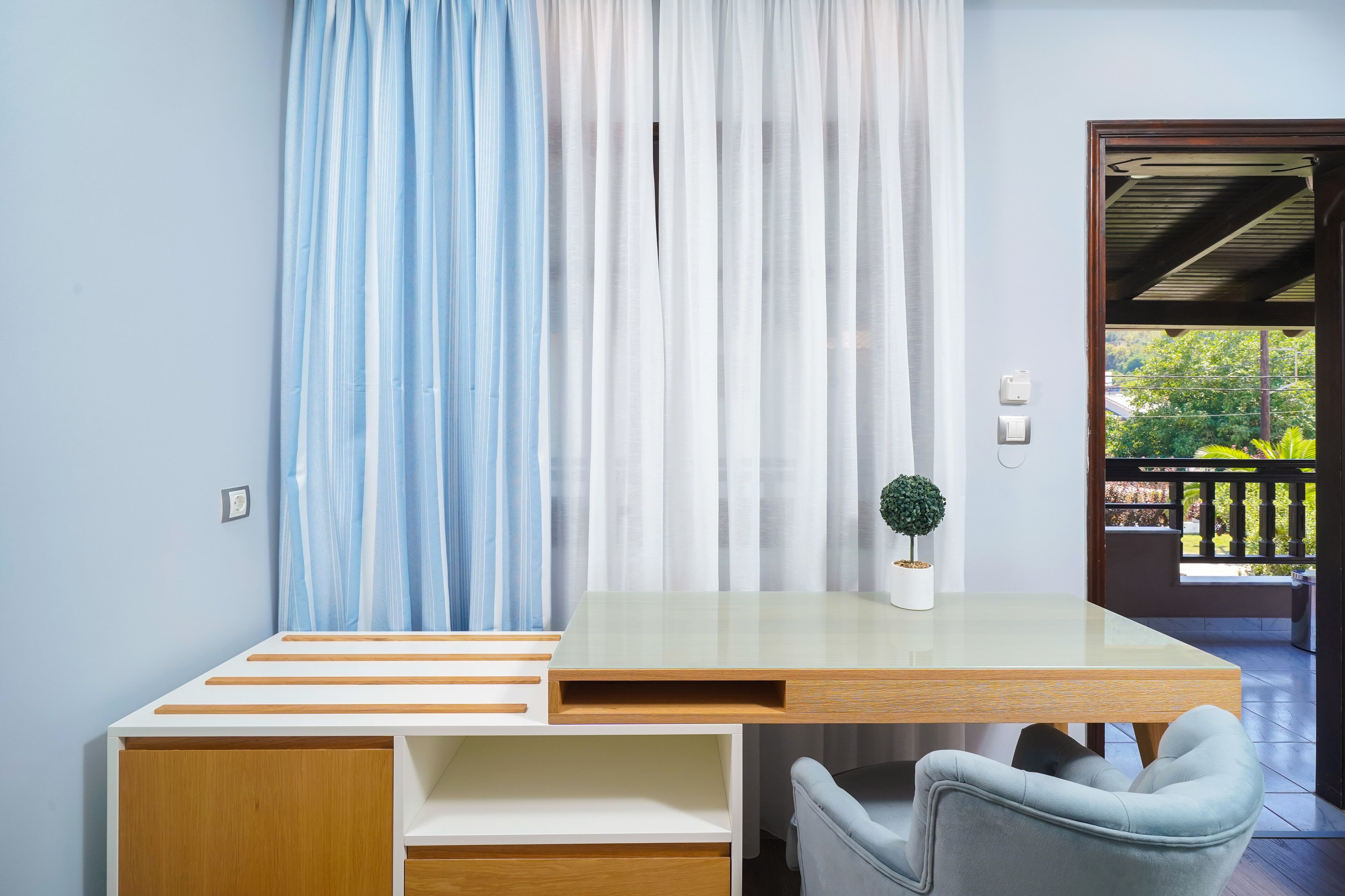 Een moderne kamer met een houten bureau, een stoel, een kleine plant in pot en uitzicht op de omgeving door een deur.