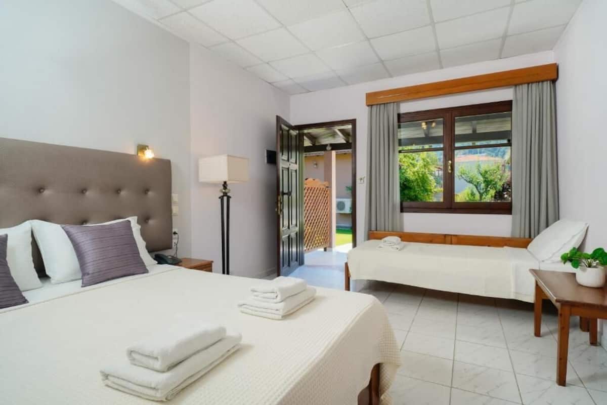 Habitación de hotel con una cama grande, otra más pequeña, una mesita de noche con lámpara y una ventana con cortinas.