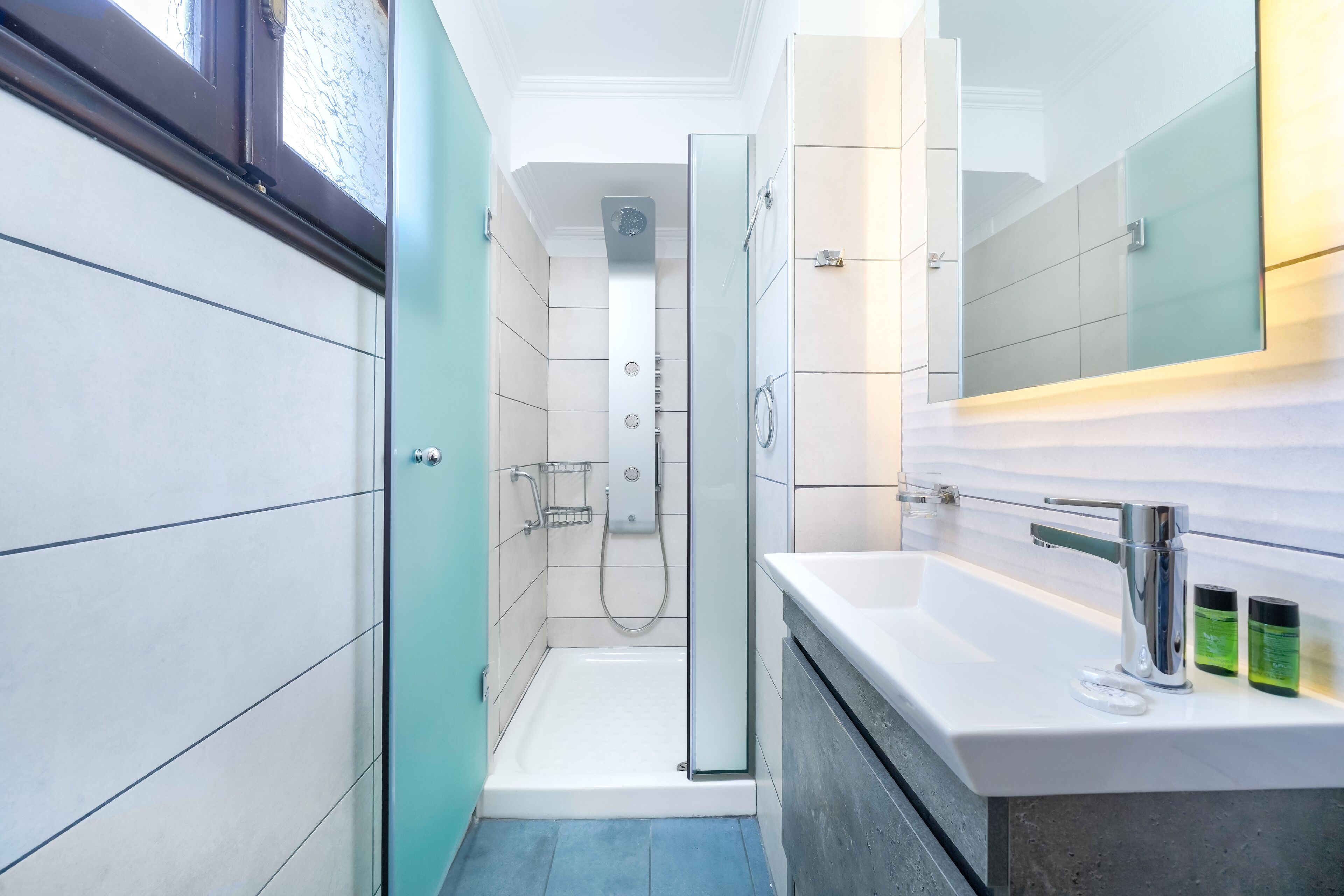 A modern bathroom with a glass shower enclosure, a white sink with a chrome faucet, and a mirror above the sink.
