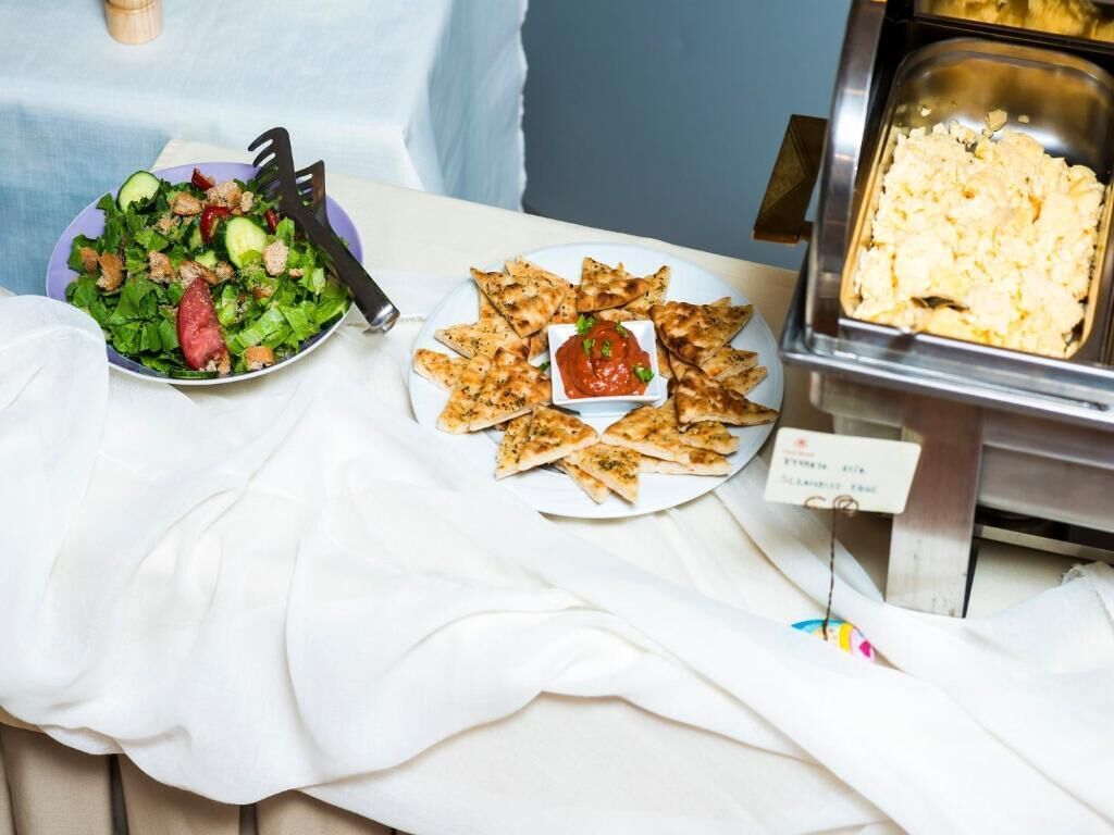 Un tavolo da buffet con insalata, pane piatto e un contenitore di purè di patate.