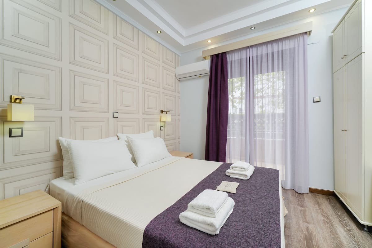 Una habitación de hotel con una cama grande, una mesita de noche, un armario y una ventana con cortinas.