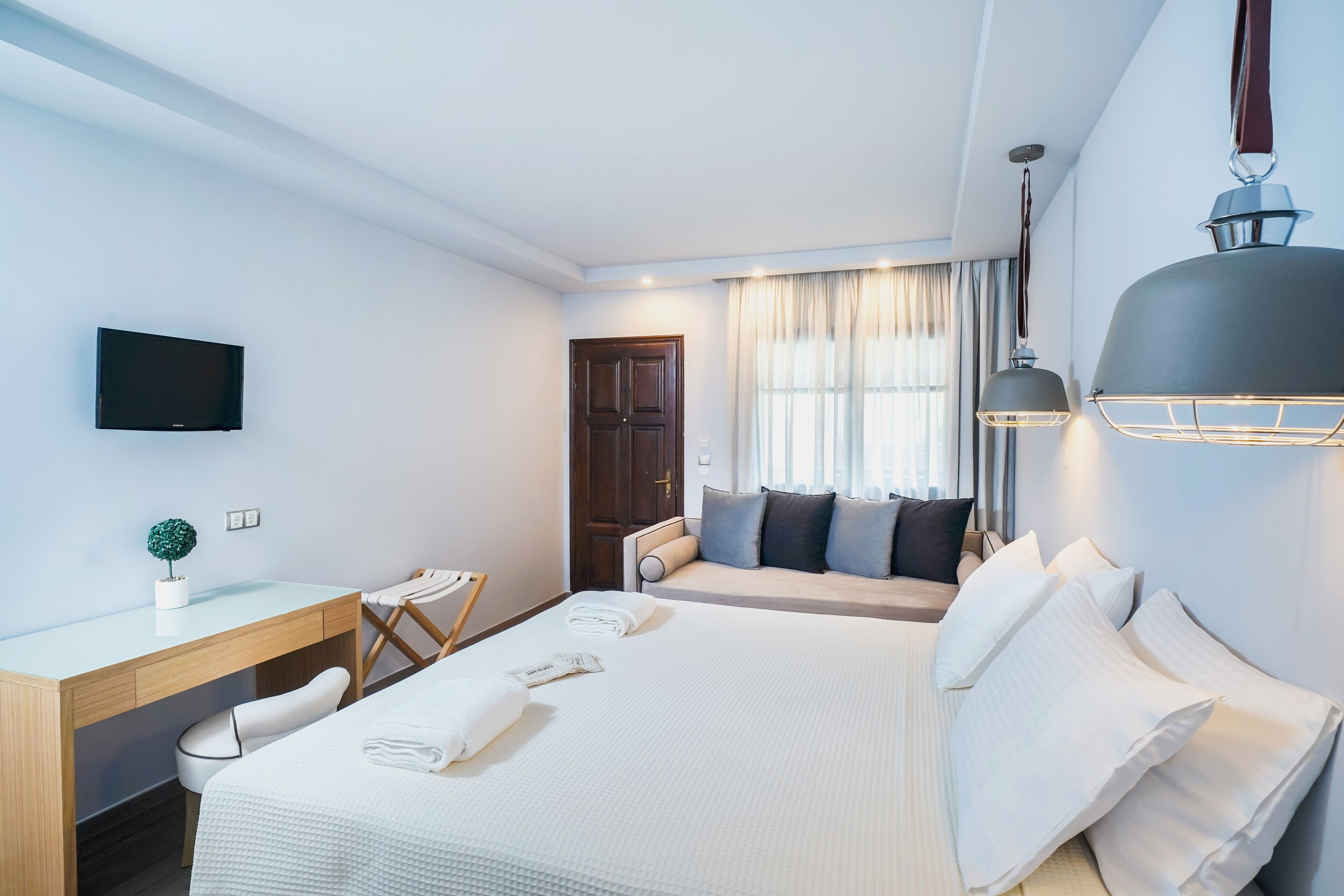 A hotel room with a bed, a desk, a chair, a television, and a window with curtains.