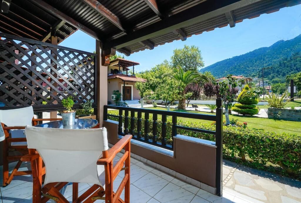 Een balkon met uitzicht op een bergachtig landschap, een betegelde vloer en een houten tafel met stoelen.