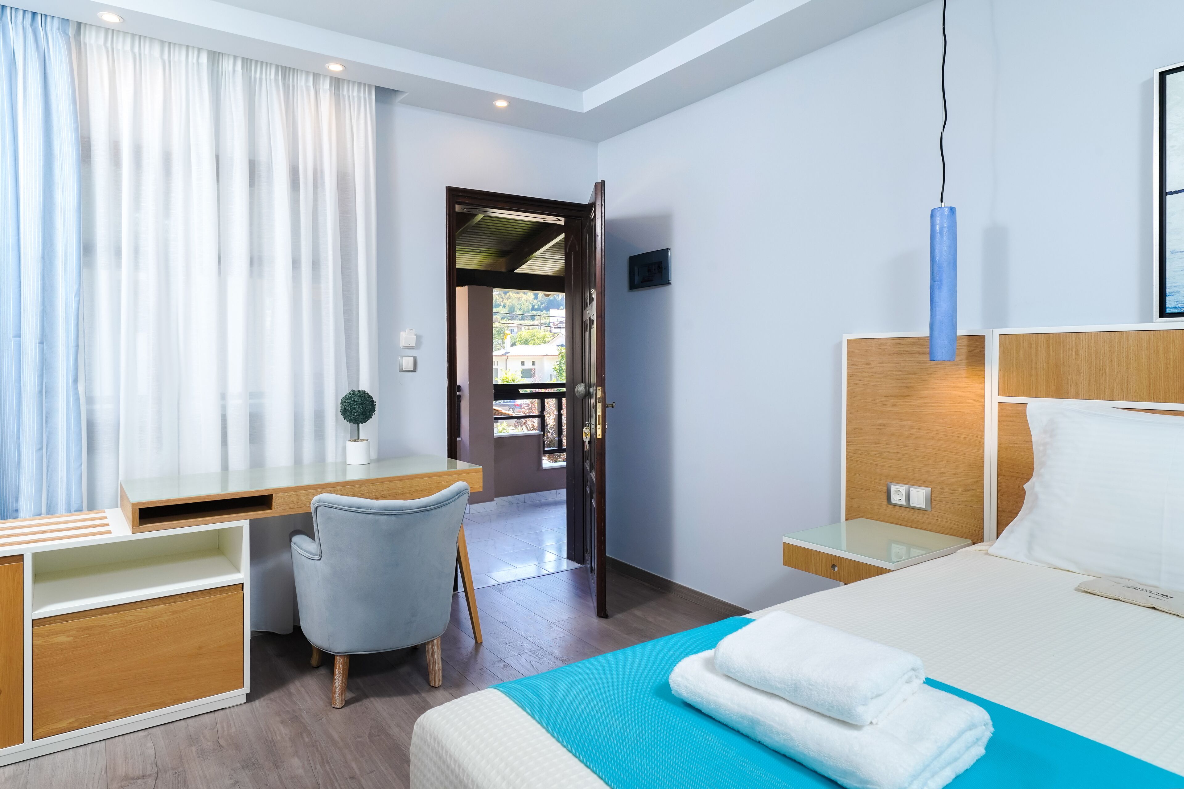 A modern hotel room with a bed, a desk, a chair, and a view of the outdoors.