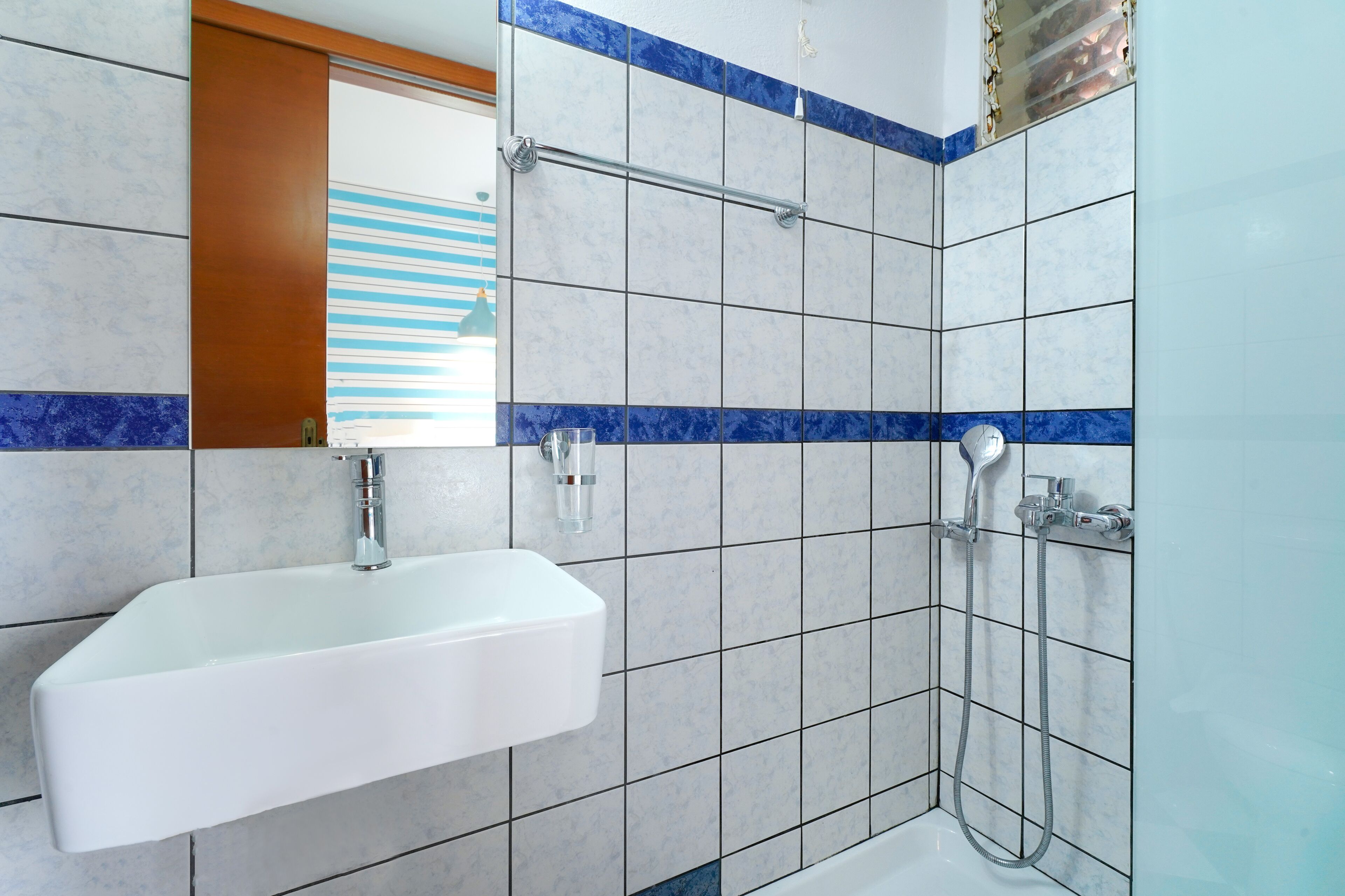 A bathroom with a white sink, a shower with a handheld showerhead, and blue-tiled walls.