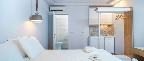 A modern hotel room with a large bed, a bedside table, a desk, and a kitchenette.