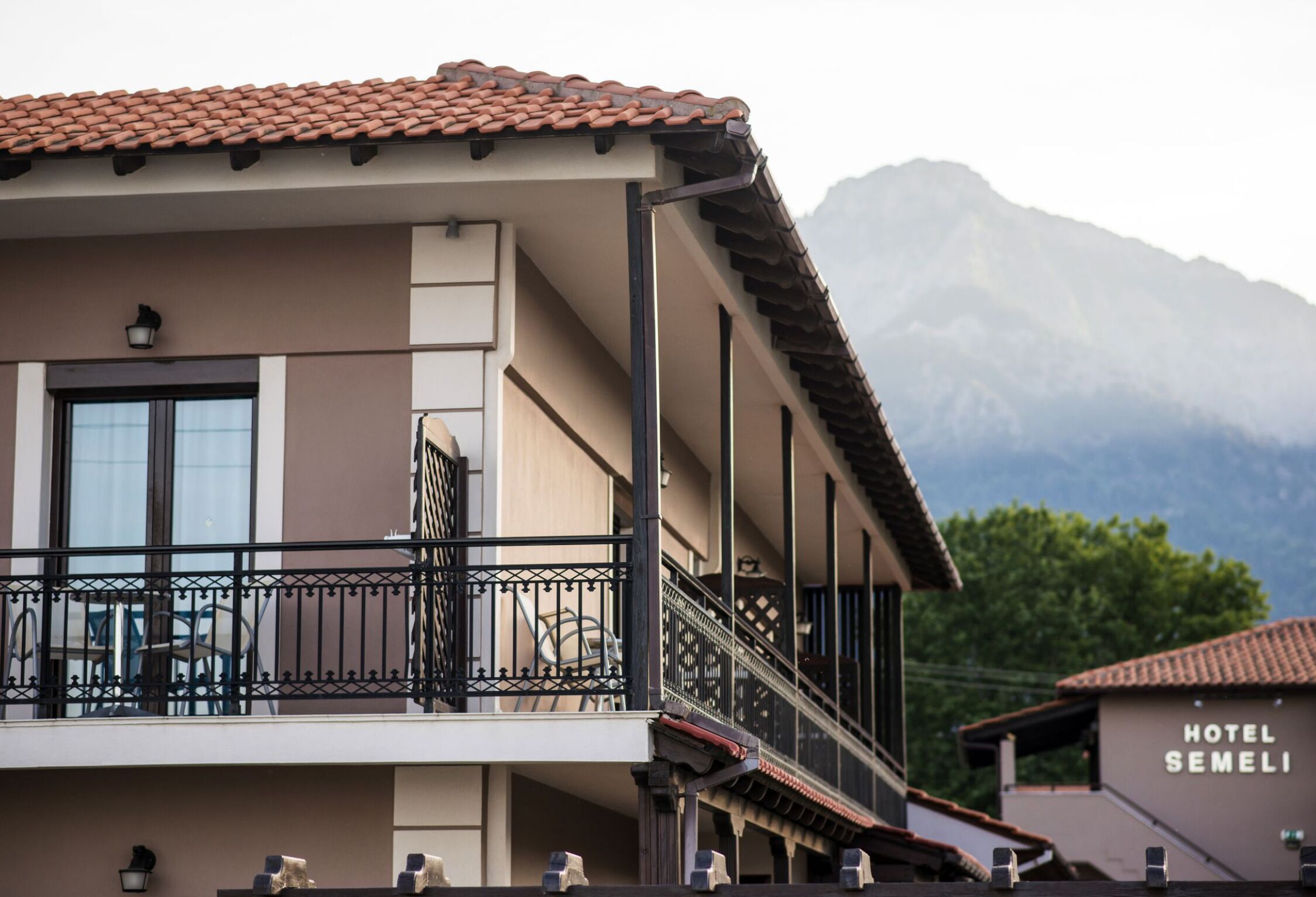 A hotel with a balcony, a mountain in the background, and a sign that reads "HOTEL SEMELI".